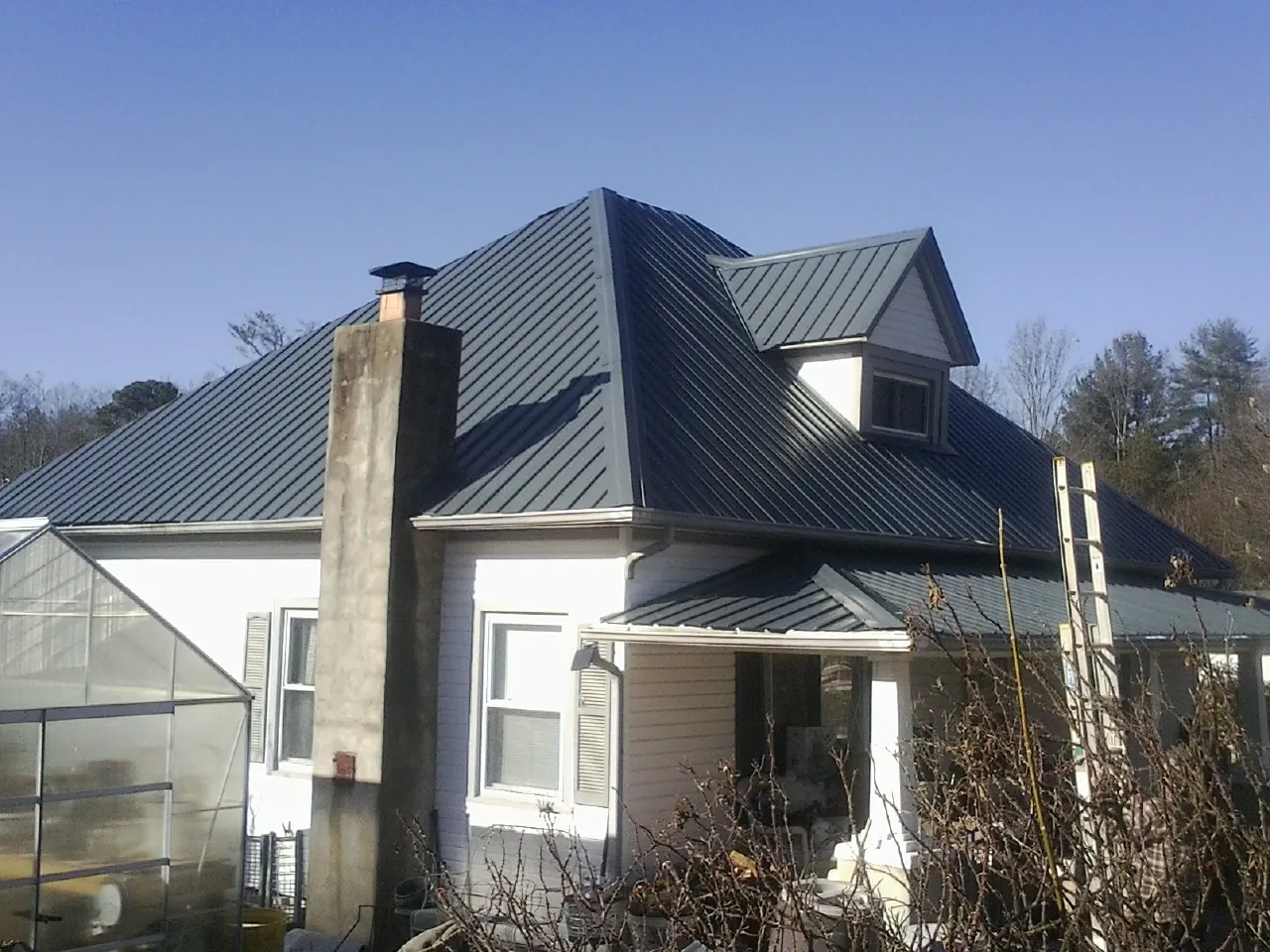 Dark blue standing seam metal roof on a white farmhouse with dormer — Slate & Tile Roof Repair by Roofing Brothers in Minocqua