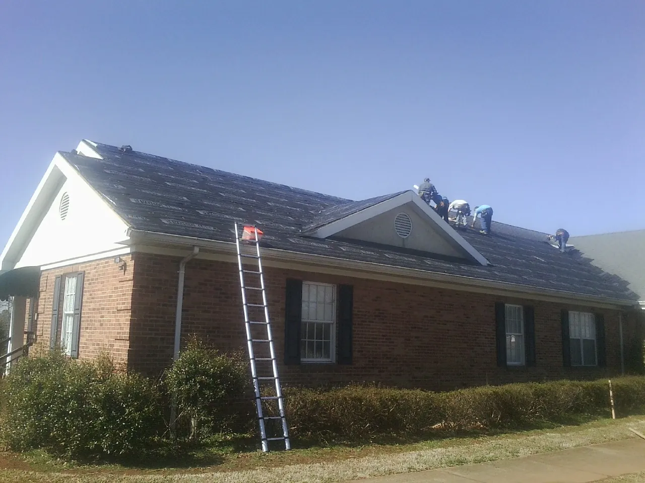 Crew tearing shingles off a brick ranch roof with a ladder set — Emergency Roof Repair work by our crew in Minocqua