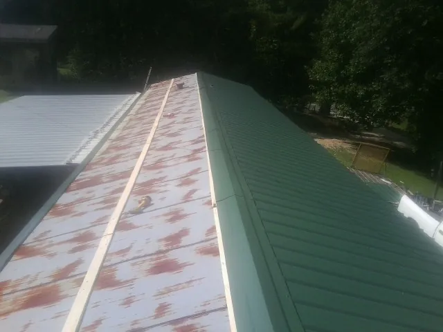 Old rusted panels beside newly installed green metal roofing — Wind Damage Roof Repair by Roofing Brothers in Minocqua