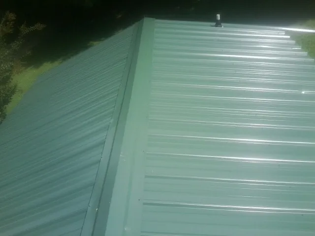 New green metal panels meeting at the ridge of a roof — Flat Roof Repair work by our crew in Minocqua