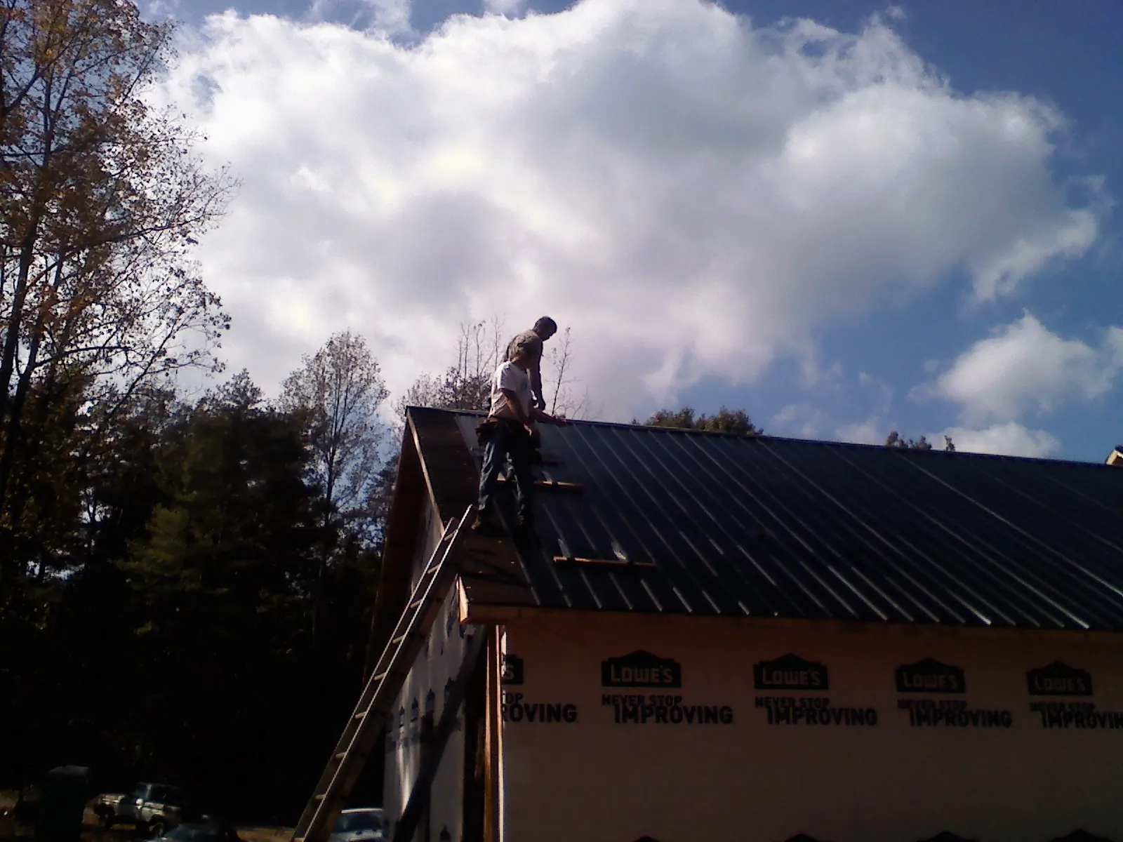 Roofer fastening dark metal panels high against a cloudy sky, from a Roof Inspection job in Minocqua