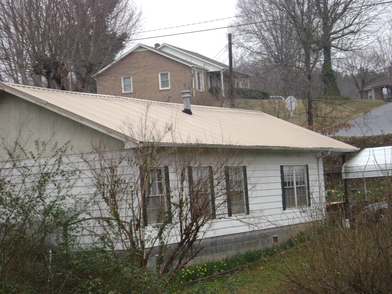 Tan metal roof on a white sided house set into a hillside — Commercial Roofing by Roofing Brothers in Minocqua